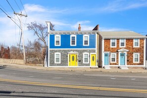 A street view with two houses, one with a blue facade and the other with a brown facade, both with white trim and multiple windows. - Trainmaster's Inn - Viking house first floor (Palmer)