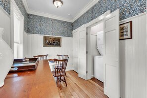 A dining area with a wooden table and chairs, a painting on the wall, and a laundry room with a washing machine. - Trainmaster's Inn - Viking house first floor (Palmer)