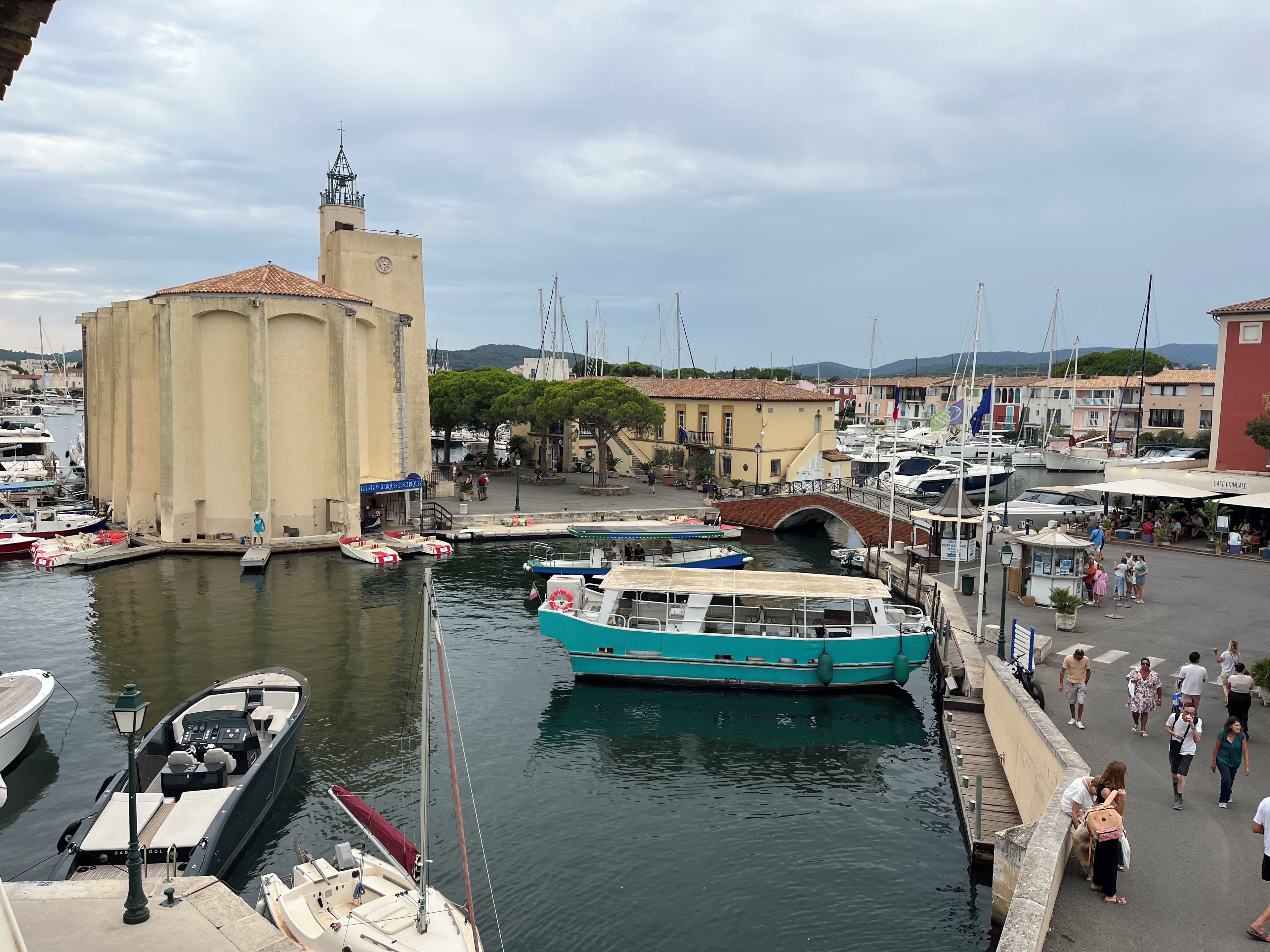 A marina with boats docked, a bridge, and buildings in the background.