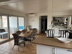 Et spiseområde med et træbord og fletstole, et køkken med moderne hårde hvidevarer, og en skydedør til en balkon.