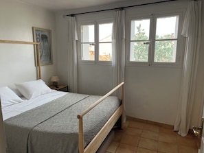 Ein Schlafzimmer mit einem Bett, einem Nachttisch, einer Lampe und einem Fenster mit Vorhängen.