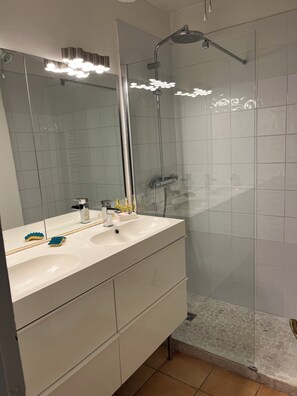 Et badeværelse med et hvidt håndvaskarrangement, et spejl og en bruseniche.