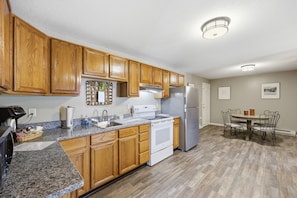 A kitchen with wooden cabinets, a stainless steel refrigerator, a built-in oven, granite countertops, and a dining area with a table and chairs. - Trainmaster's Inn - 1294 South Main, Apt 2 (Palmer)