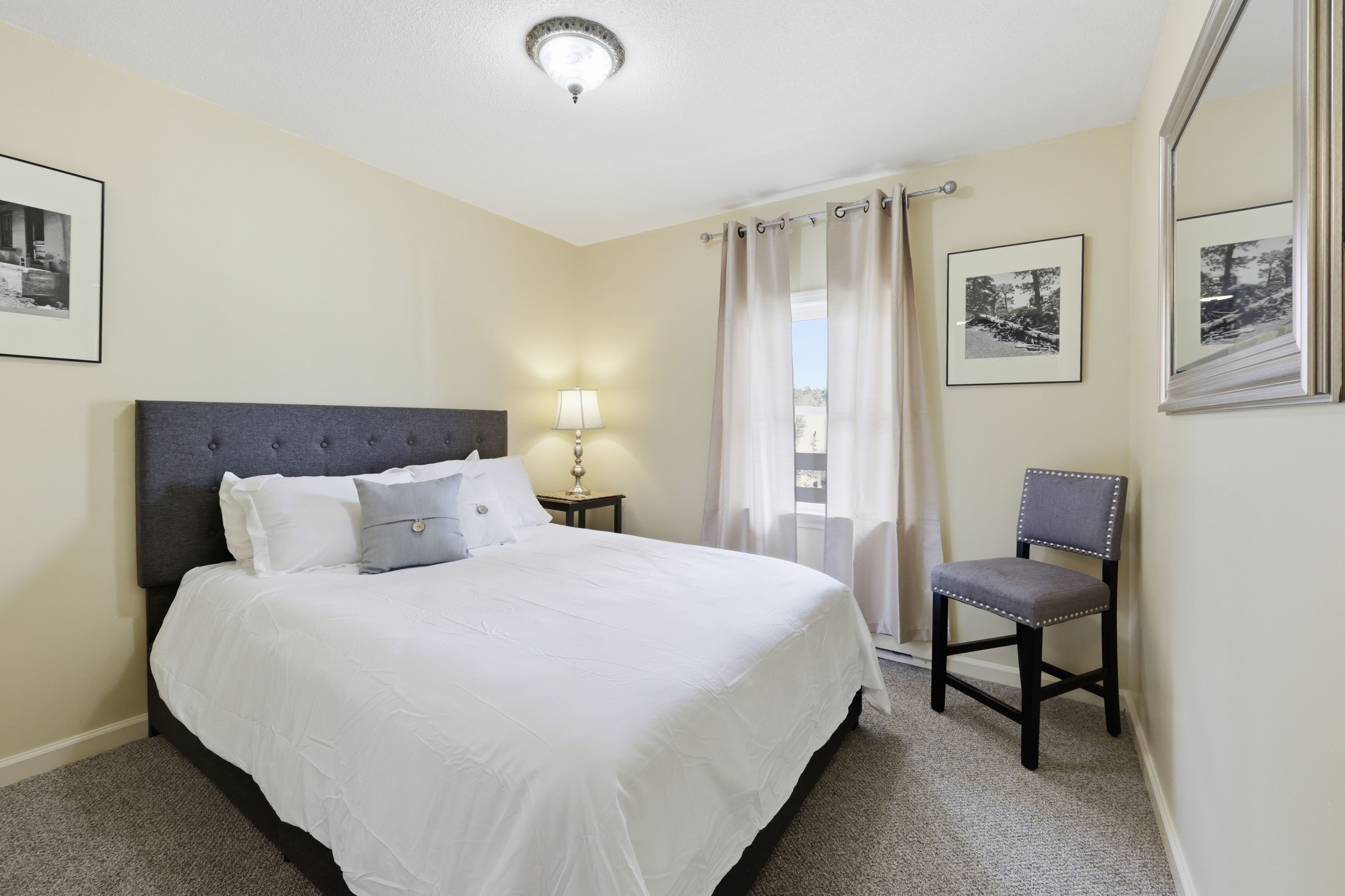Een hotelkamer met een groot bed, een stoel, een nachtkastje, een lamp en twee ingelijste foto's aan de muur.