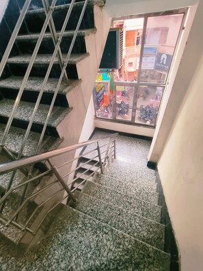 A staircase with metal railings leading to a ground floor area with a glass door and window, allowing views of the street outside. - Kashi Gulab Homestay (Varanasi)