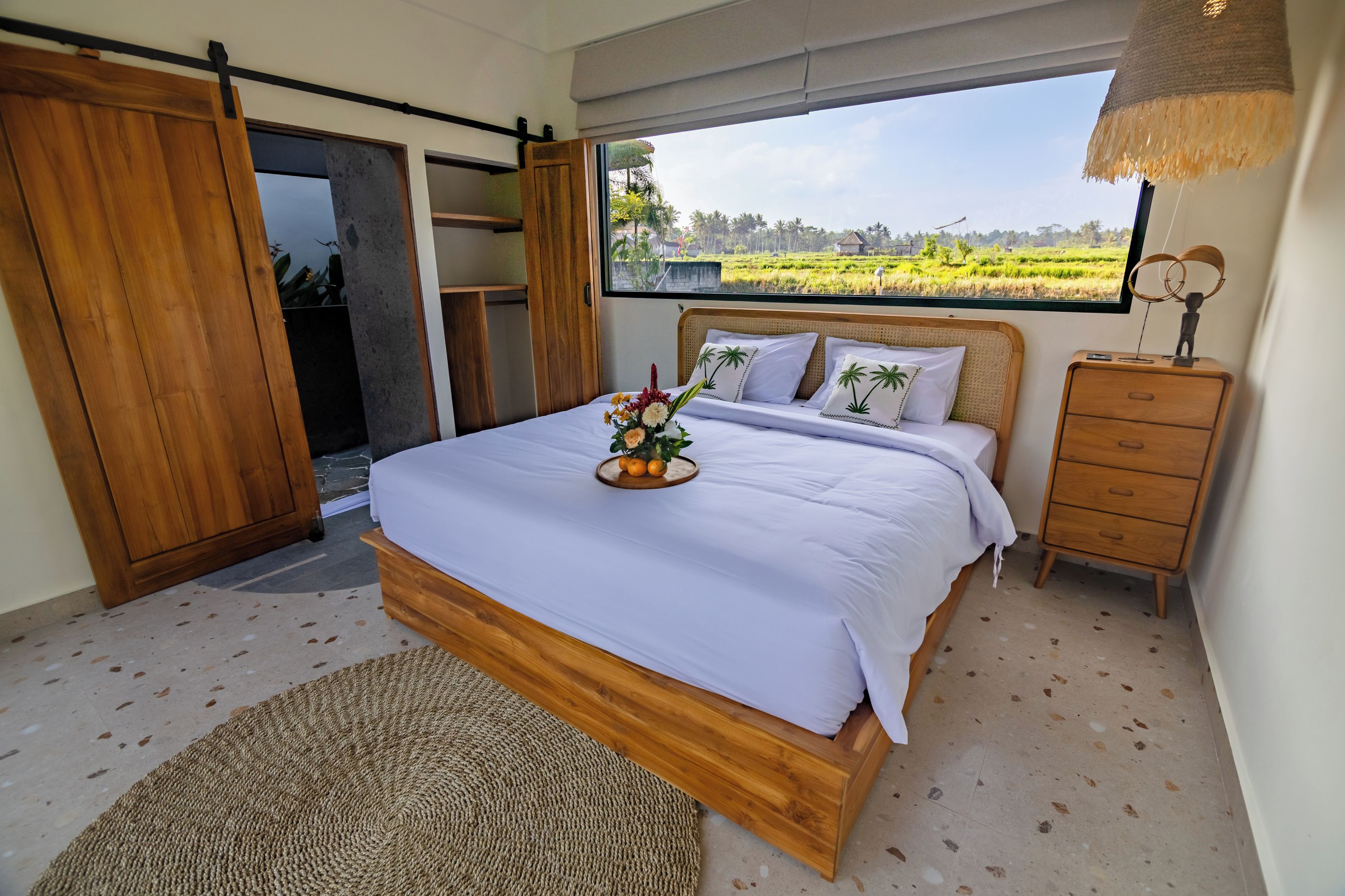 Quarto com cama, cômoda de madeira, janela com vista para um campo e porta deslizante.