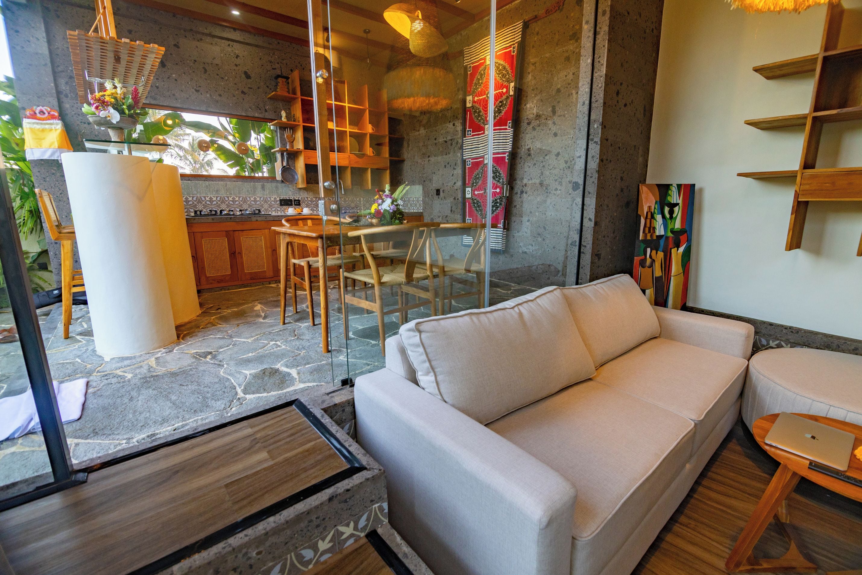 Una sala moderna con un sofá, un comedor con una mesa y sillas, y una cocina con estufa y estanterías.