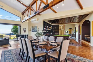Une salle à manger spacieuse avec un haut plafond et des poutres apparentes, une table de billard et une vue sur l’extérieur.