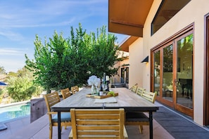 An outdoor dining area with a wooden table and chairs, surrounded by greenery and a pool. - Private Pool + Hot Tub + Snooker | 42-Acre Vineyard | The Villa at Ambyth Estate (Templeton)