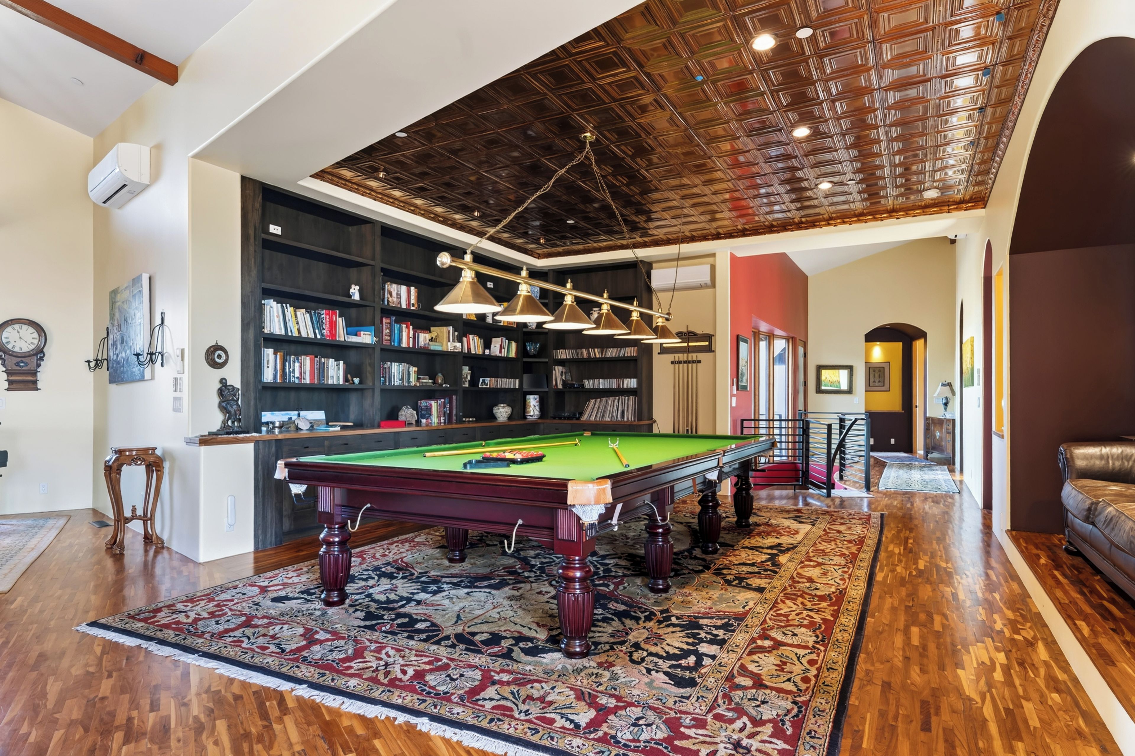 A billiards room with a pool table, bookshelves, and a decorative ceiling.