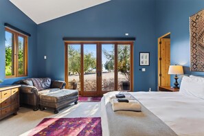 Une chambre avec un grand lit, un canapé, un bureau et une vue sur l’extérieur, accessible par une porte-fenêtre coulissante.