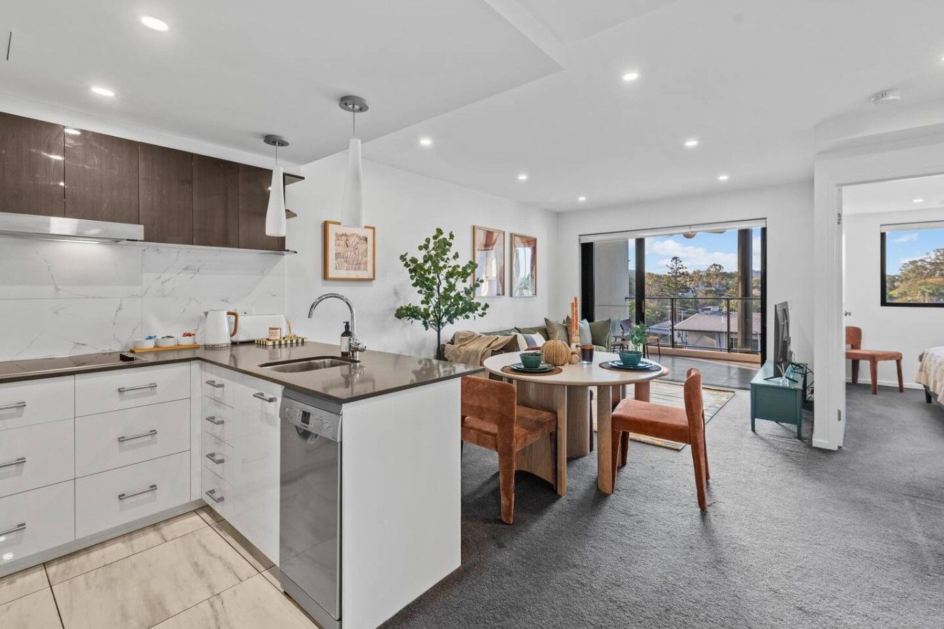 A modern kitchen with a central island, a dining area with a round table, and a large window offering a view.