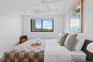 Un dormitorio moderno con una cama grande, un ventilador de techo, una ventana con vistas y un cuadro en la pared.