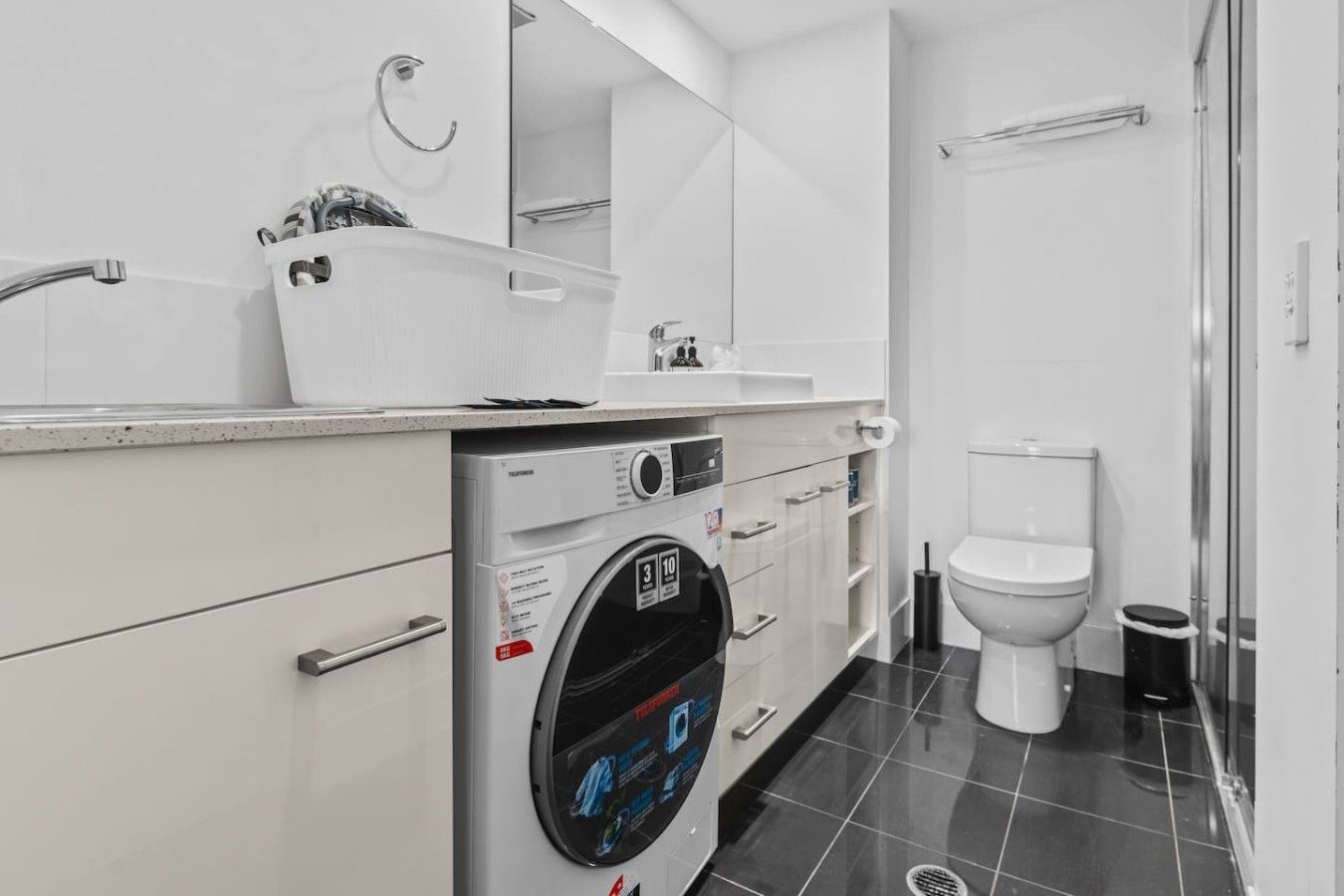 A modern bathroom with a washing machine, toilet, and a glass shower enclosure.