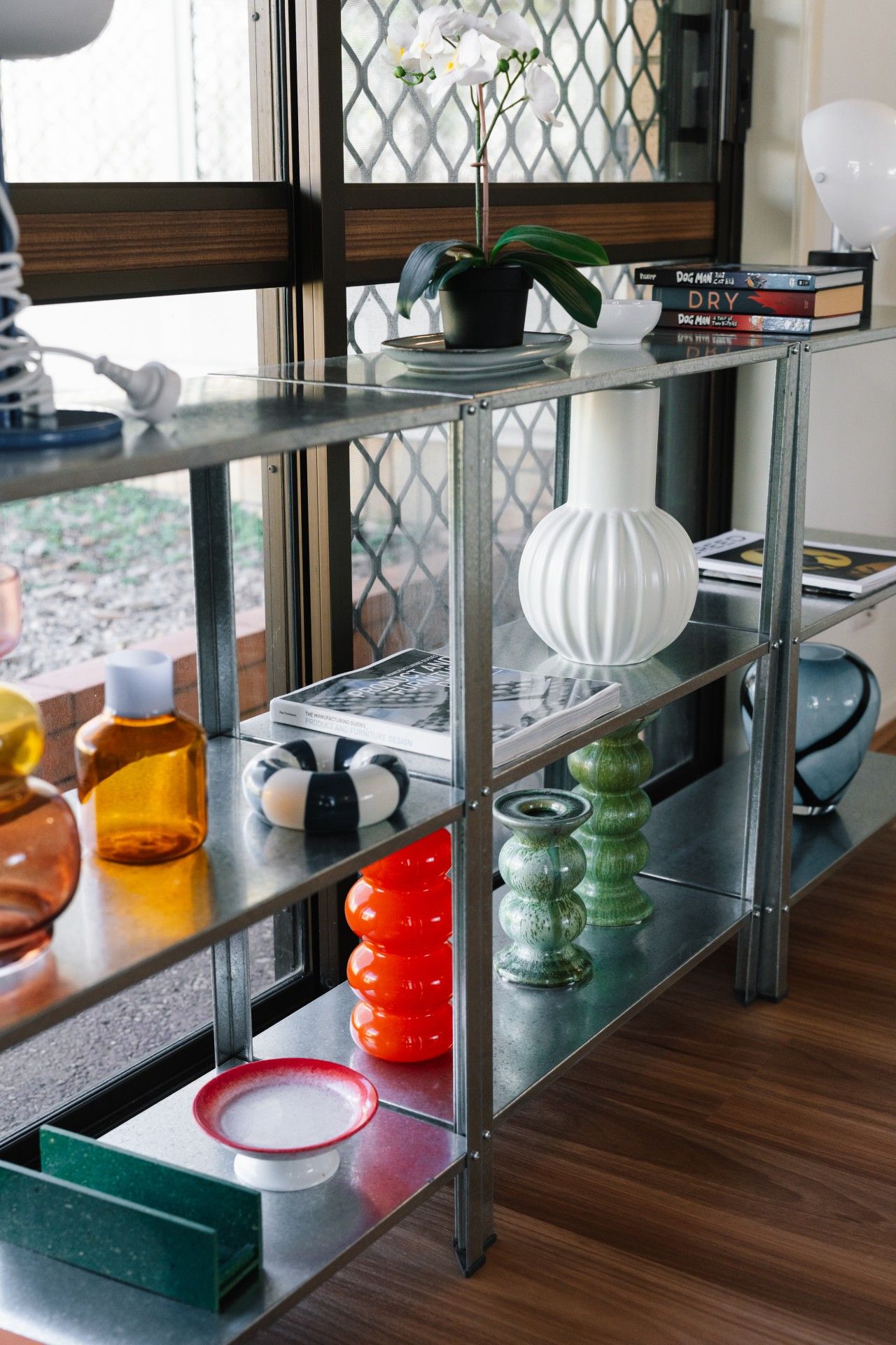 A metal shelf unit with various decorative items including a potted orchid, books, and colorful vases.