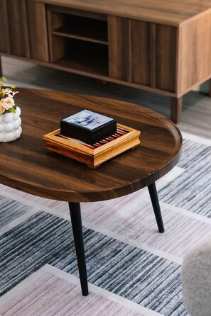 A wooden coffee table with a black object on it, a white vase with flowers, and a striped rug. - Brand New4BR Home |Aircon Every Bedroom |GoodValue (White Rock)