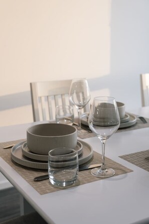 Une table à manger dressée avec des assiettes, des bols et des verres, et une chaise en arrière-plan.