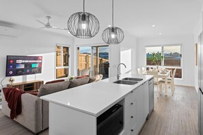 A modern kitchen with a central island, a dining area with a table and chairs, and a TV mounted on the wall. - Brand New4BR Home |Aircon Every Bedroom |GoodValue (White Rock)