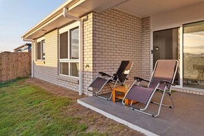 A house with a brick exterior, a covered patio with two lounge chairs, and a wooden table. - Brand New4BR Home |Aircon Every Bedroom |GoodValue (White Rock)
