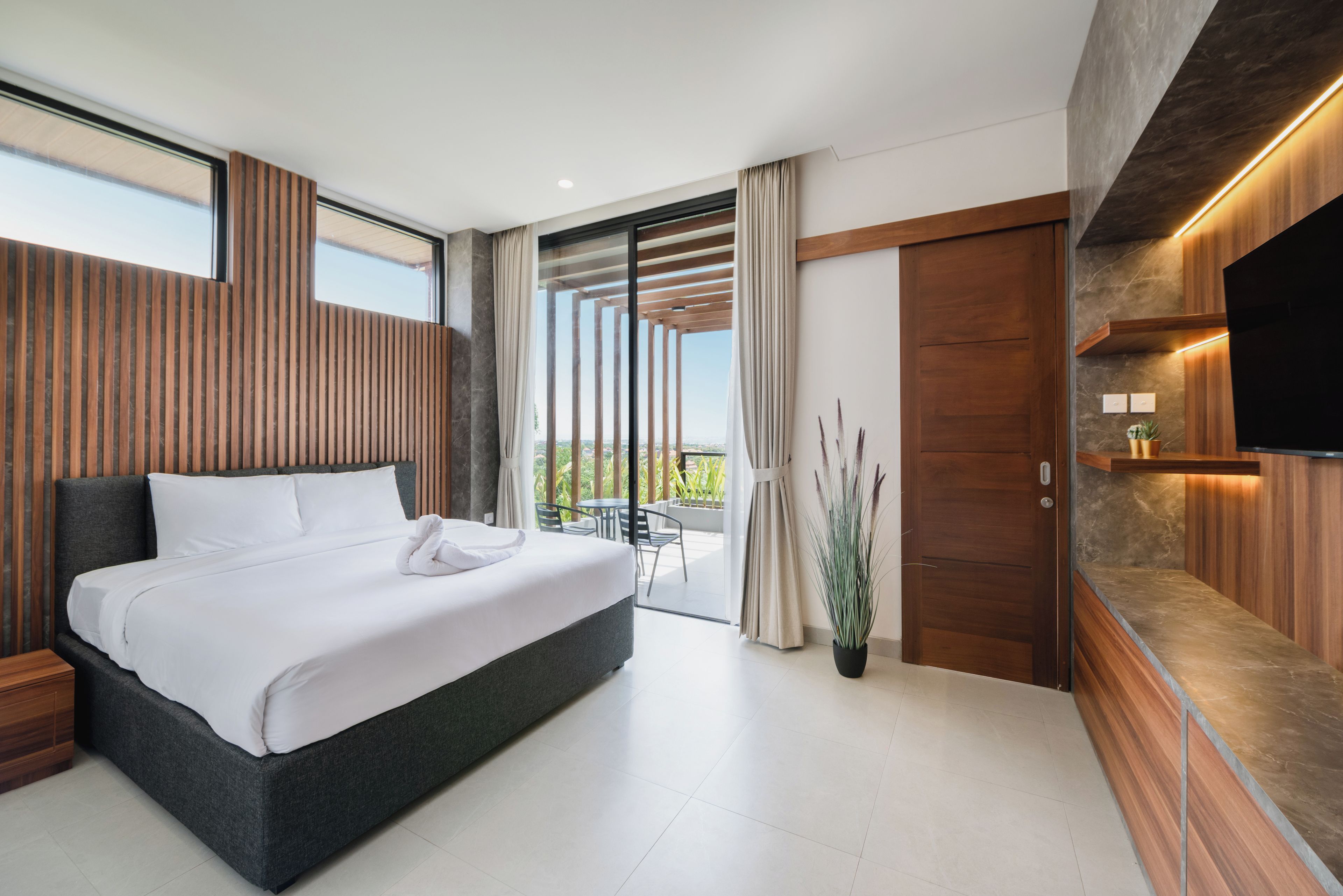 Ein modernes Hotelzimmer mit einem großen Bett, einem Balkon mit Blick und einem an der Wand befestigten Flachbildfernseher.
