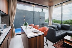 A modern kitchen with a marble countertop, a dining area with orange chairs, and a grey sofa.