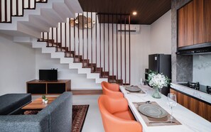 A modern living room with a sofa, a coffee table, and a dining area with orange chairs and a white table.