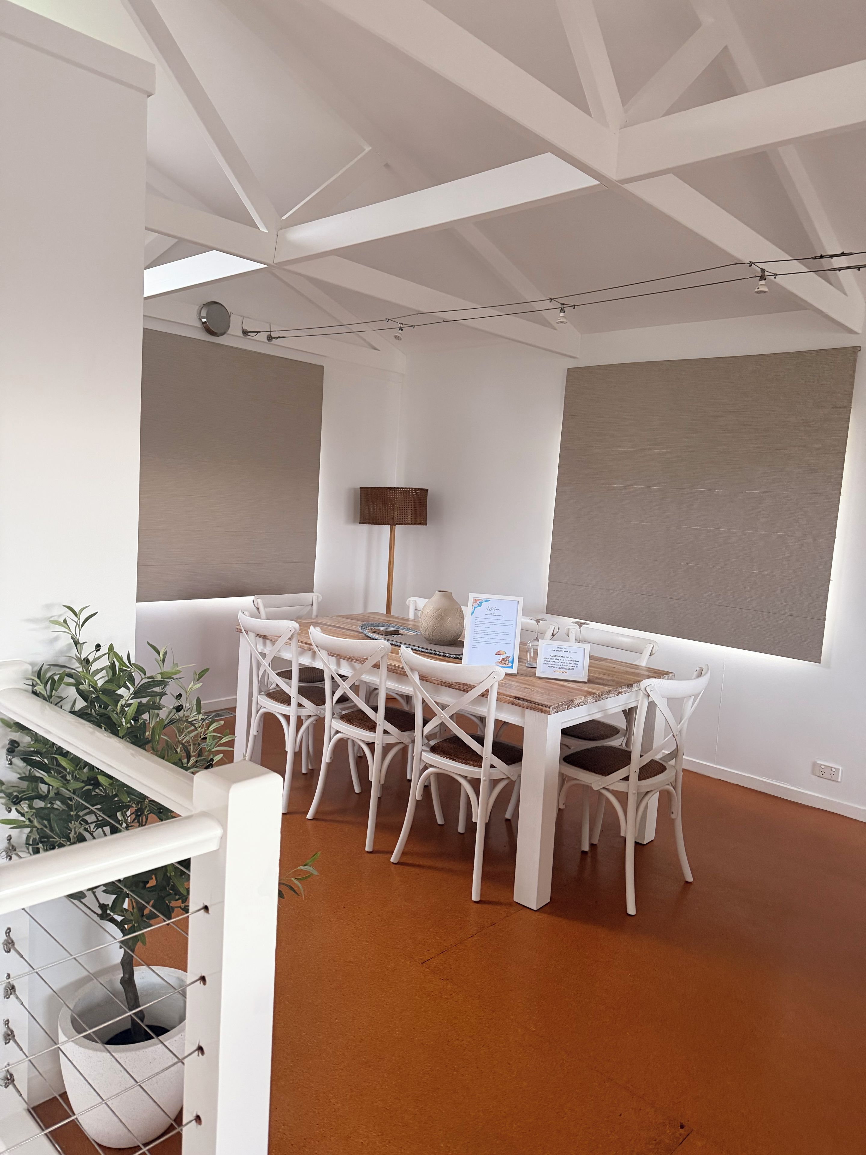 Un comedor con mesa de madera, sillas blancas, un jarrón y un letrero con el menú.