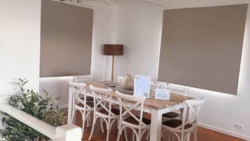 Un comedor con mesa de madera, sillas blancas, un jarrón y un letrero con el menú.