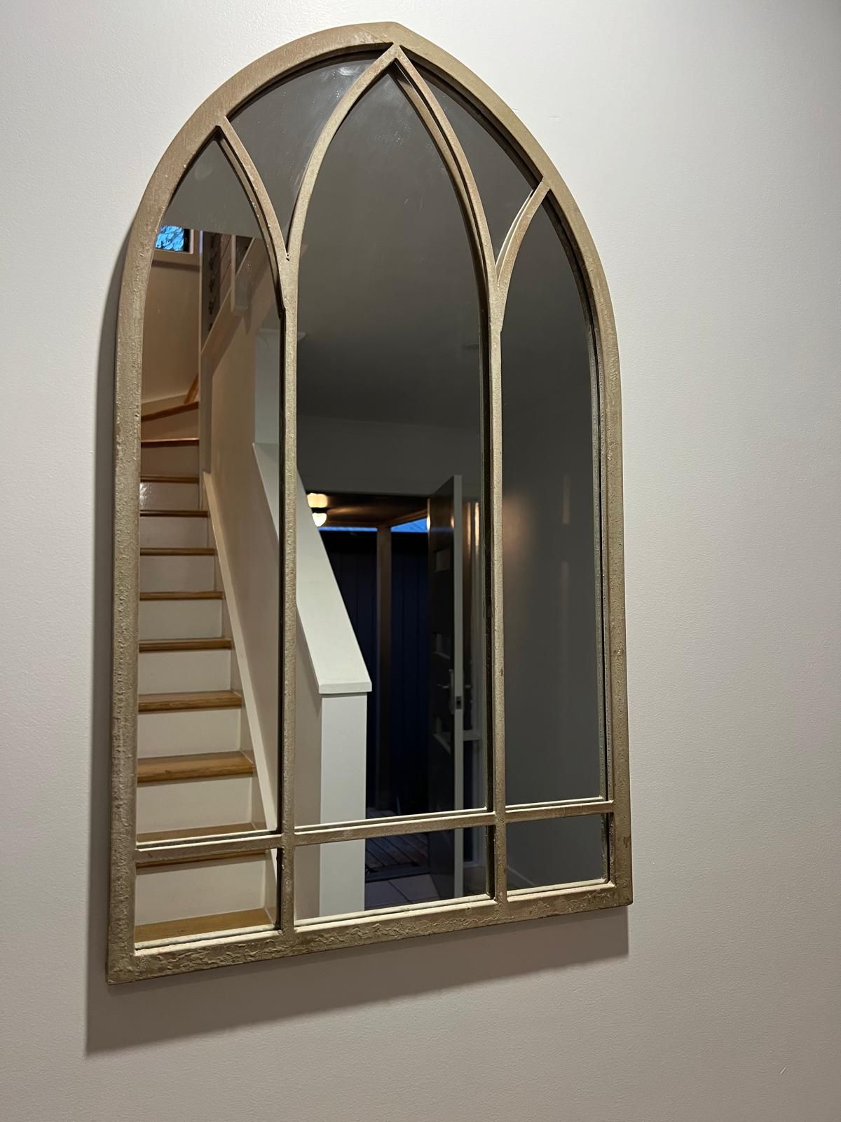 Un espejo montado en la pared con un diseño de arco gótico.
