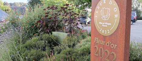 A sign with 'Fleur d'Or 2022' and 'Villes et Villages Fleuris' text, surrounded by greenery and flowers.
