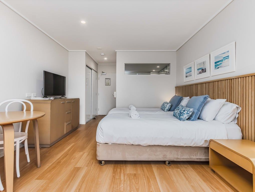 Un dormitorio moderno con una cama, mesita de noche y televisor sobre un aparador.