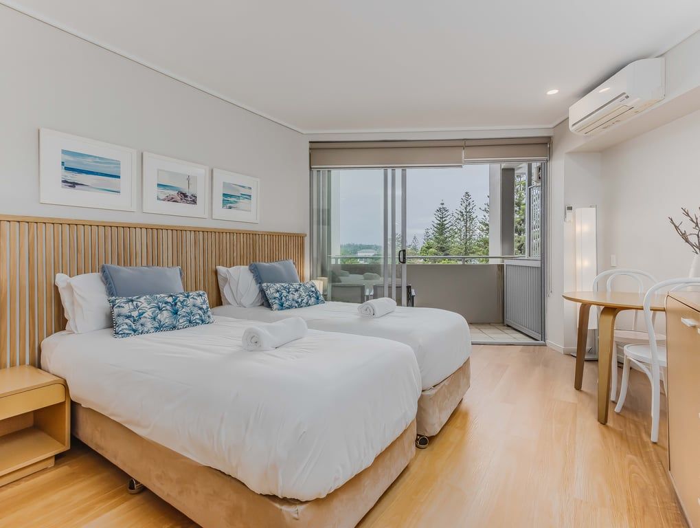 Une chambre d’hôtel moderne avec deux lits, un balcon et un coin repas.