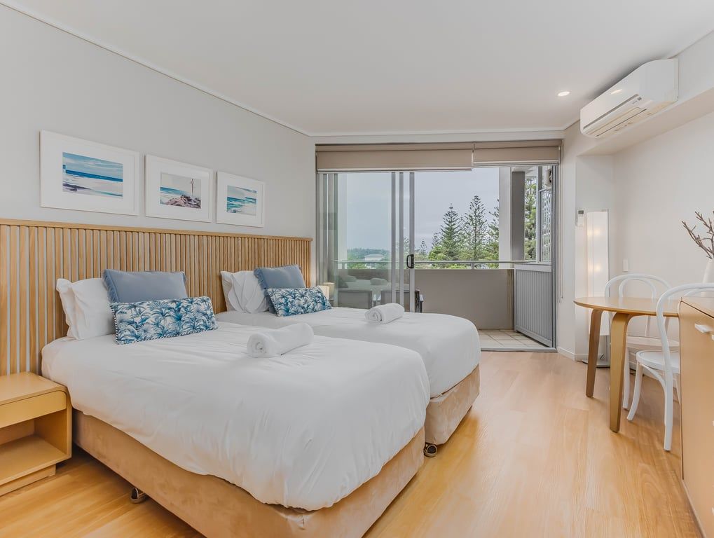 A modern hotel room with two beds, a balcony, a dining area, and artwork on the wall.