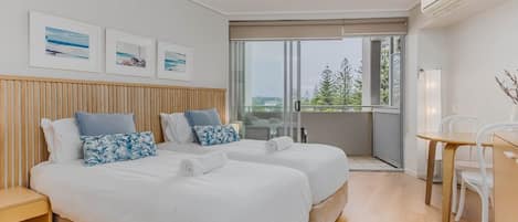 A modern hotel room with two beds, a balcony, a dining area, and artwork on the wall.