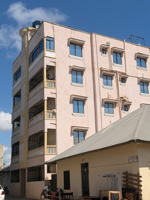 Un edificio de varios pisos con balcones, techo plano y un letrero que indica un espacio comercial.