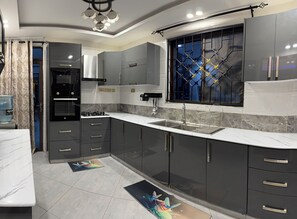 A modern kitchen with grey cabinets, a built-in oven, a sink, and a decorative window with a geometric pattern. - Modern Haven Ultimate Coastal Getaway, Modern & Serene (Mombasa)
