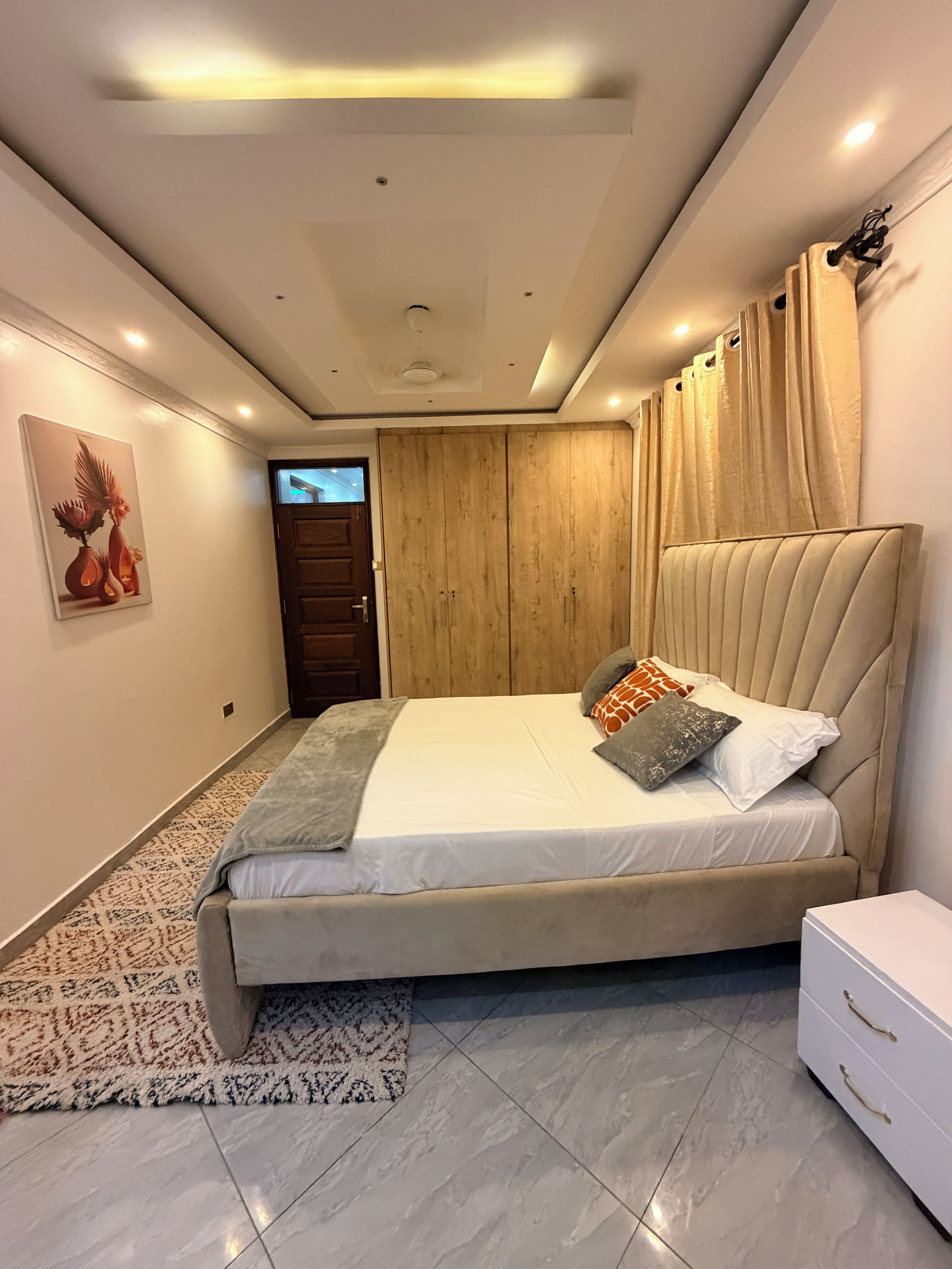 A bedroom with a bed, a nightstand, a wardrobe, a patterned rug, and a painting on the wall.