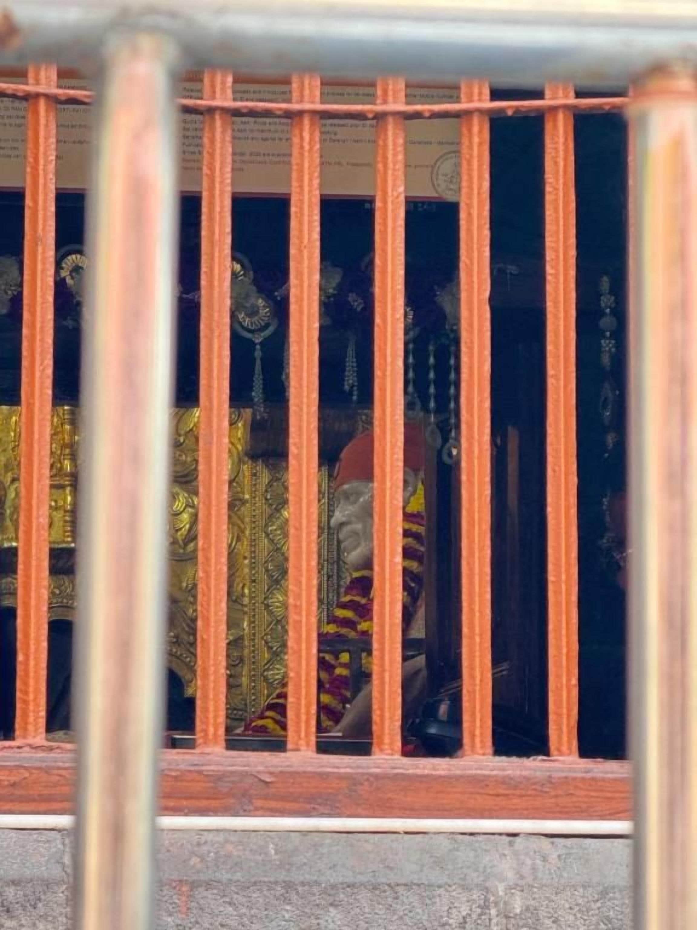 Una ventana con barrotes, por donde se distingue un tejido estampado y una figura vestida con atuendo tradicional.