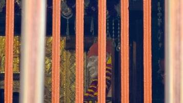 Una ventana con barrotes, por donde se distingue un tejido estampado y una figura vestida con atuendo tradicional.