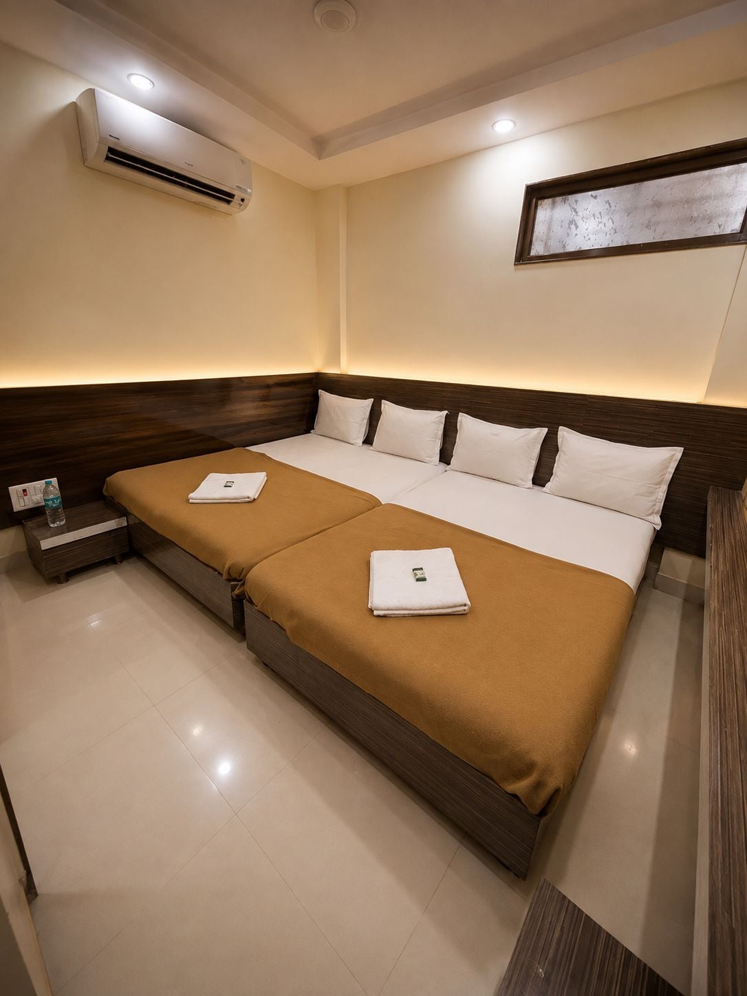 A hotel room with a large bed, two bedside tables, an air conditioning unit, and a wall-mounted light fixture.