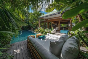 A poolside area with a wooden deck, a covered seating area, and lush greenery. - Bawa House (Pererenan)