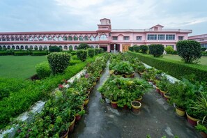 A building with a central courtyard, surrounded by neatly arranged potted plants and a well-maintained lawn. - Omji Ashram - Udasin Sangat Rishi (Ayodhya)