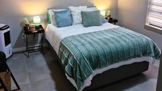 A bedroom with a bed, nightstands, a heater, and wall art. - TrueStar at TrueNorth (Pretoria)