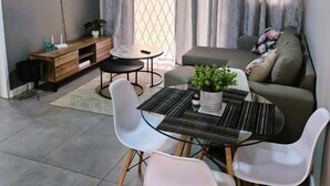 A modern living room with a dining table, chairs, a sofa, and a TV mounted on the wall. - TrueStar at TrueNorth (Pretoria)