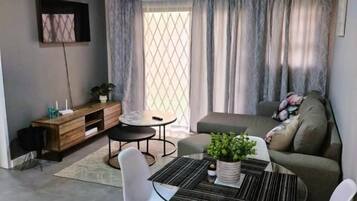 A modern living room with a dining table, chairs, a sofa, and a TV mounted on the wall.