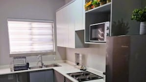 A compact kitchen with a built-in microwave, a stainless steel refrigerator, and a window with blinds. - TrueStar at TrueNorth (Pretoria)