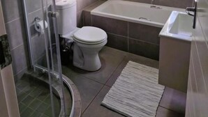 A bathroom with a glass shower enclosure, a toilet, a bathtub, and a sink. - TrueStar at TrueNorth (Pretoria)