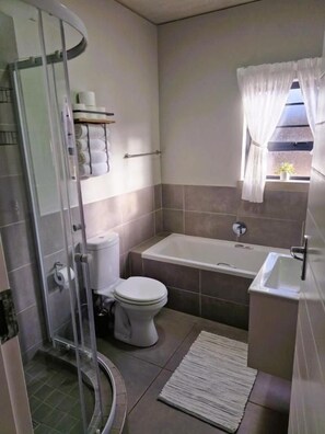 A bathroom with a glass shower enclosure, a toilet, a bathtub, and a sink. - TrueStar at TrueNorth (Pretoria)