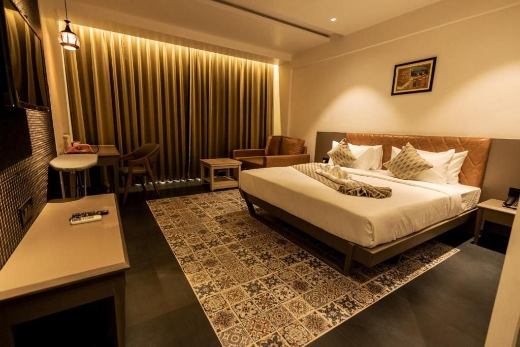 A hotel room with a bed, bedside table, chair, and a desk with a remote control.