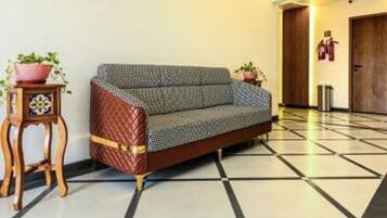 A room with a sofa, a small wooden table with a plant, and a tiled floor.